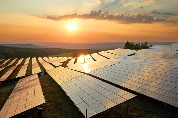 Placas solares en el campo con el cielo atardeciendo y el sol incidiendo sobre ellas